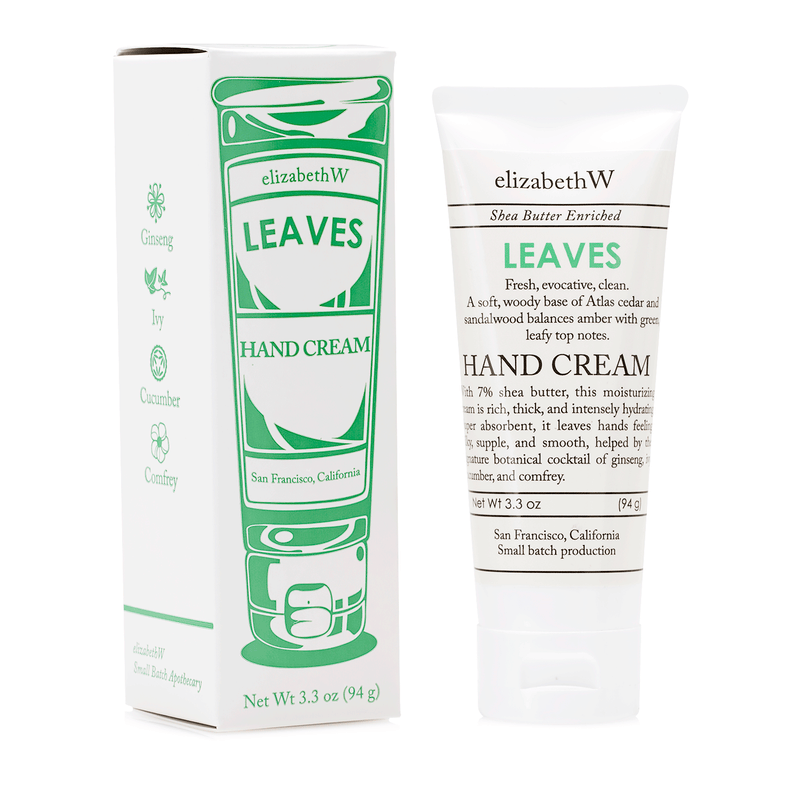 A product image featuring Elizabeth W Small Batch Apothecary Leaves Hand Cream in a white tube with green designs, alongside its matching packaging box. The packaging highlights natural ingredients like ginseng, cucumber, and shea butter.