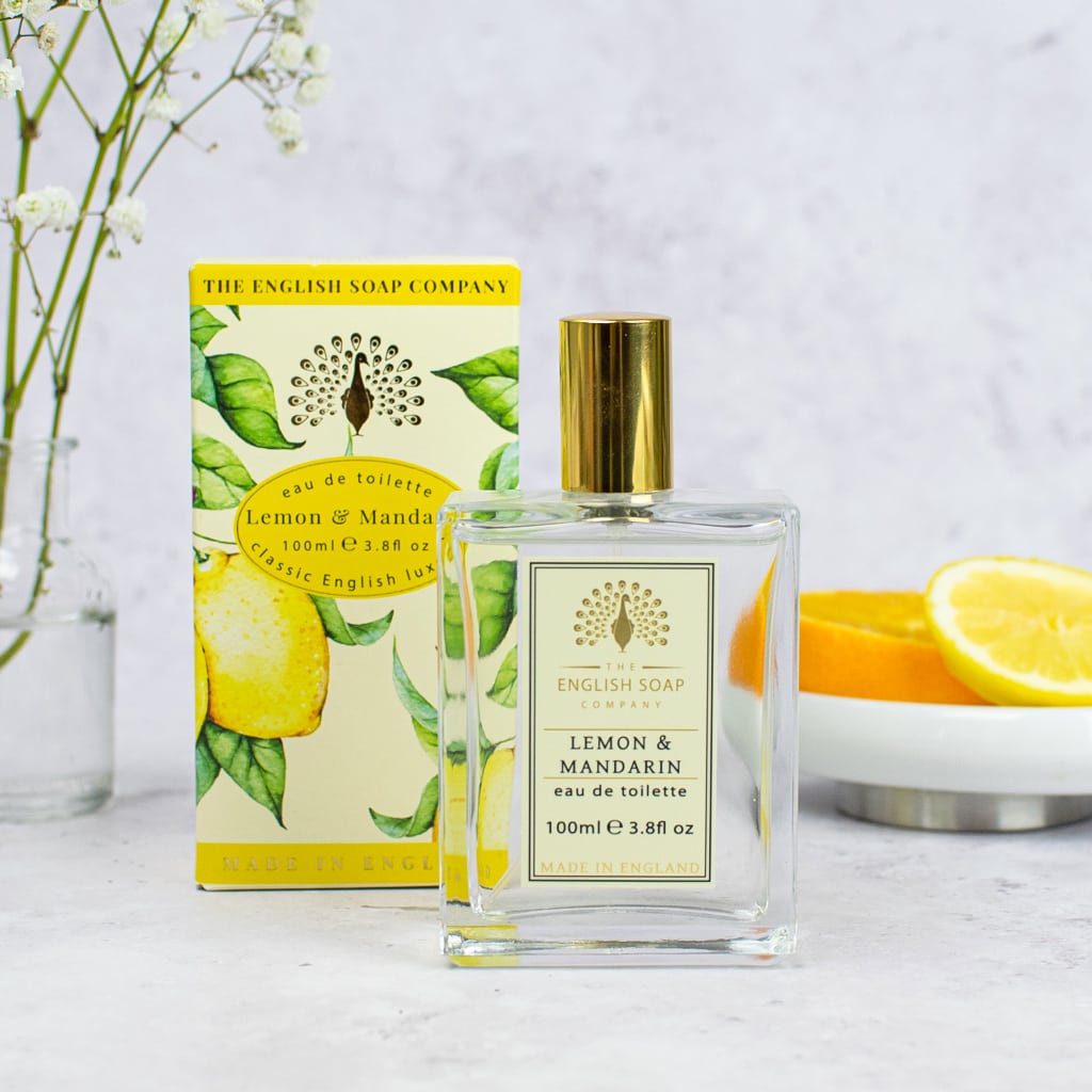 A bottle of The English Soap Co. Vintage Lemon & Mandarin EDT next to its sustainable packaging, with slices of fresh lemon and a floral background.