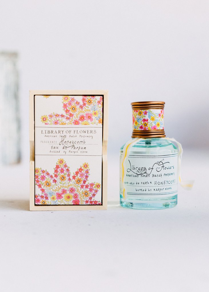 A Margot Elena Library of Flowers Honeycomb Eau De Parfum bottle and its packaging, both adorned with vibrant, colorful flower designs, displayed against a soft white background.