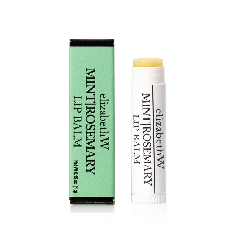 A nourishing elizabeth W Purely Essential Mint Rosemary Lip Balm next to its green packaging box on a white background. The tube is uncapped, and the balm is slightly raised.
