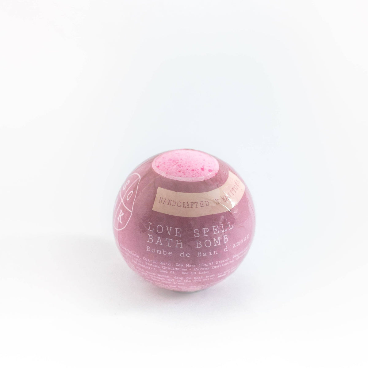 A pink, spherical bath bomb labeled "SOAK Bath Co. - Love Spell Bath Bomb" in elegant text, placed against a white background.