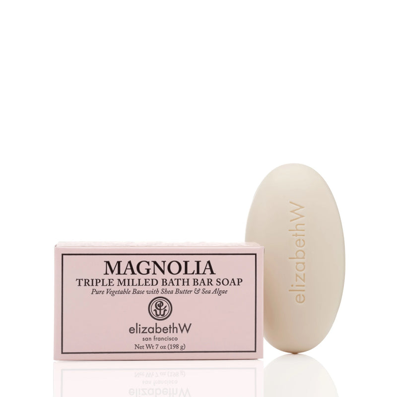 A bar of elizabeth W Signature Magnolia Bath Bar - 7oz, made with plant-based ingredients, beside its pink packaging box, both labeled, on a white background.