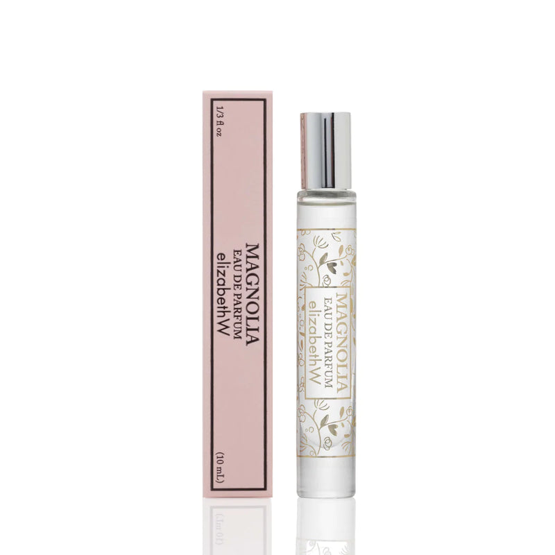 A bottle of Elizabeth W Signature Magnolia Rollerball next to its pink packaging box on a white background. The bottle has a metallic silver spray top and features elegant floral designs.