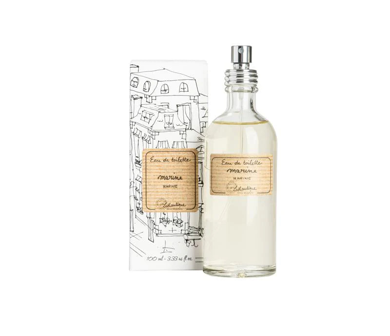 A clear glass bottle of Lothantique Marine EDT White Package next to its illustrated packaging. The label and box feature elegant, handwritten-style text and sketches of city buildings.