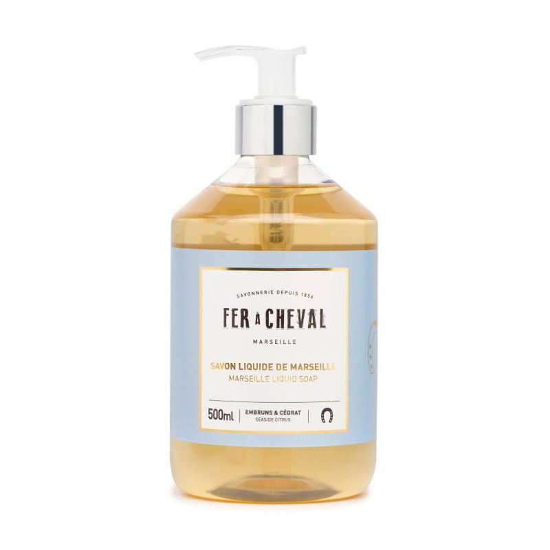 A clear plastic pump bottle containing 500ml of Fer à Cheval Marseille liquid soap enriched with coconut oil, featuring a light amber color and a white pump top, labeled in blue and white.