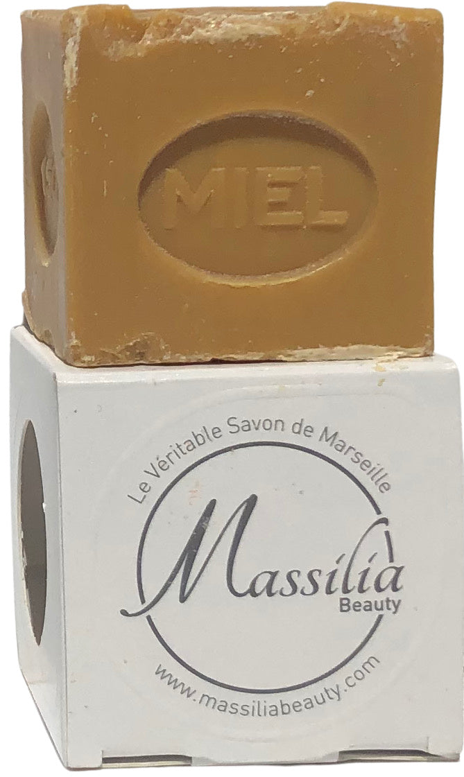 A cube of honey-scented Made in Provence soap labeled "miel" on top, resting on its branded cardboard packaging from "Massalia Beauty.
