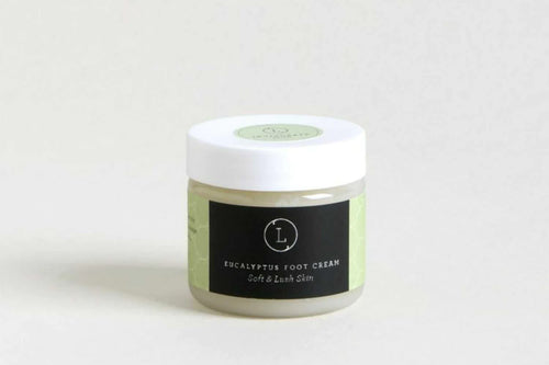 A jar of Lizush Eucalyptus Shea Butter Foot Cream labeled "soft & lush skin" placed against a plain light background. The jar has a green and black label with a minimalist design.