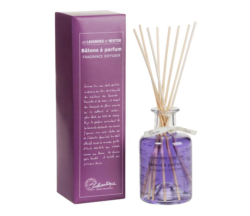 A purple box labeled "Lothantique Les Lavandes de Nestor Fragrance Diffuser" beside a clear glass reed diffuser bottle with lavender fragrance oil and several reed sticks. The box