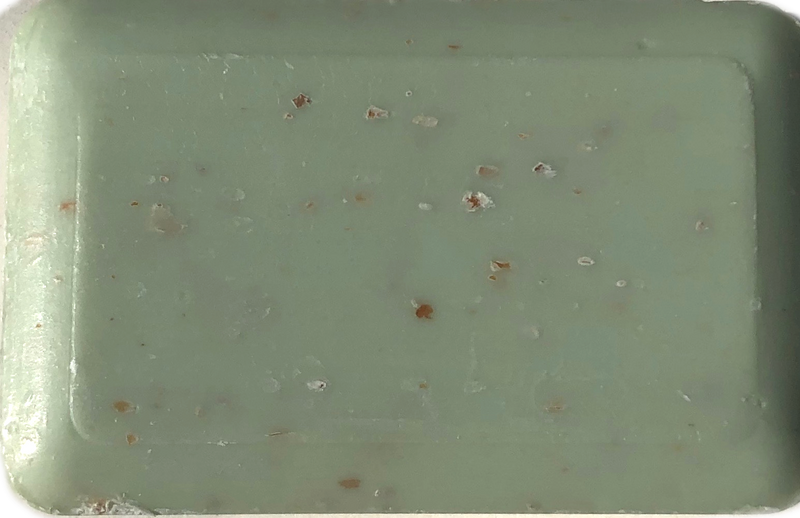 An empty light green plastic tray with small La Lavande Ocean Broyee w/seaweed soap crumbs scattered across its surface.