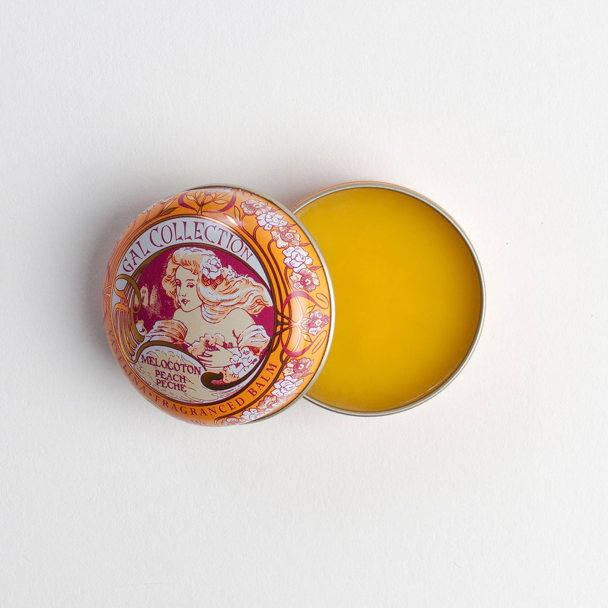 An open round tin of Perfumeria Gal Madrid fragranced lip balm in peach displaying a vintage floral design on the lid, with visible yellow-colored perfume inside against a white background.