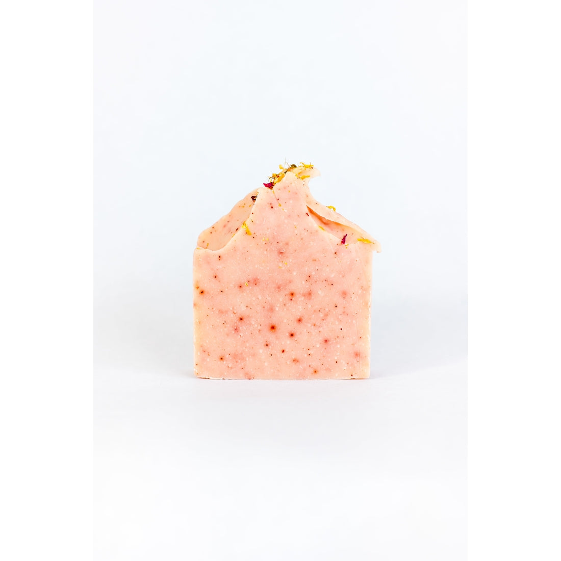 A handmade SOAK Bath Co. - Peony Soap Bar with a pale pink hue sprinkled with dried flower petals, positioned against a plain white background.
