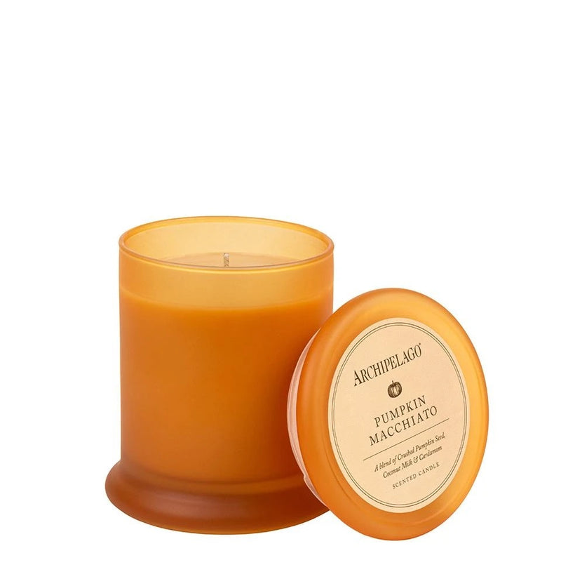 A pumpkin-colored scented candle in a glass container next to its matching lid with the label "Archipelago Botanicals, Archipelago Pumpkin Macchiato Jar Candle - Ltd Edition." The background is white.