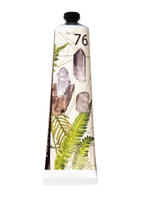 A tube of TokyoMilk Radiant Gem No. 76 Bon Bon Shea Butter Lotion, enriched with Shea Butter, featuring a nature-inspired design with illustrations of crystals, fern leaves, and numeric elements on a white background by Margot Elena.