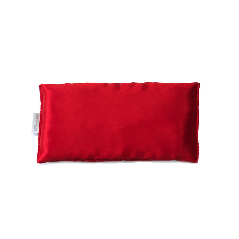 A vibrant red rectangular elizabeth W Silk Eye Pillow with a soft texture, isolated on a white background. A fabric tag is visible on one side.
