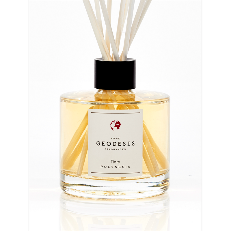 A clear, square glass diffuser bottle labeled "Geodesis Tiare Reed Diffuser" with light yellow liquid and several reed sticks inserted, exuding a Polynesian tiare flower scent, set against a white