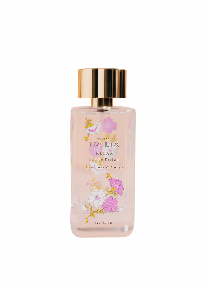 A transparent glass bottle of Margot Elena's Lollia Relax Eau de Parfum with a gold cap, labeled "lavender bee blossom honey" with floral designs, against a white background.