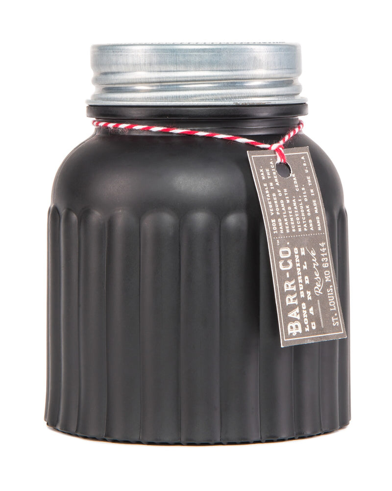 A black, ribbed Barr-Co. Reserve Apothecary Jar Candle with a silver lid, tied with a red and white string attached to a label reading "Barr-Co. fine handmade scented candles," against a white background.