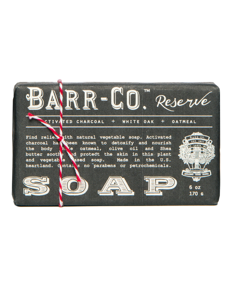 A Barr-Co. Reserve Triple-Milled Bar Soap wrapped in twine, featuring activated charcoal, white oak, and oatmeal, packaged in a black box with vintage-style white typography. Made from pure vegetable soap.