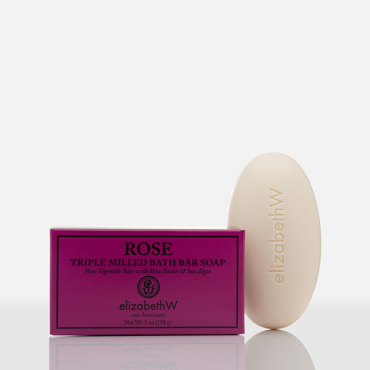 A bar of Elizabeth W Signature Rose Soap - 7oz next to its vibrant pink packaging labeled "rose" from elizabeth W, on a reflective white surface.