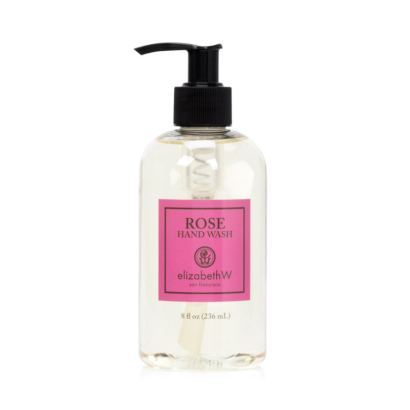 A transparent bottle of elizabeth W Signature Rose Hand Wash with a black pump dispenser, labeled in pink and styled with white and black text describing wild roses. The background is pure white.