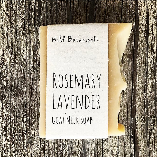 A bar of "Wild Botanicals Rosemary Lavender Soap" with shea butter by Wild Botanicals, placed on a rustic wooden surface. The label is simple and elegant, with clear black text.