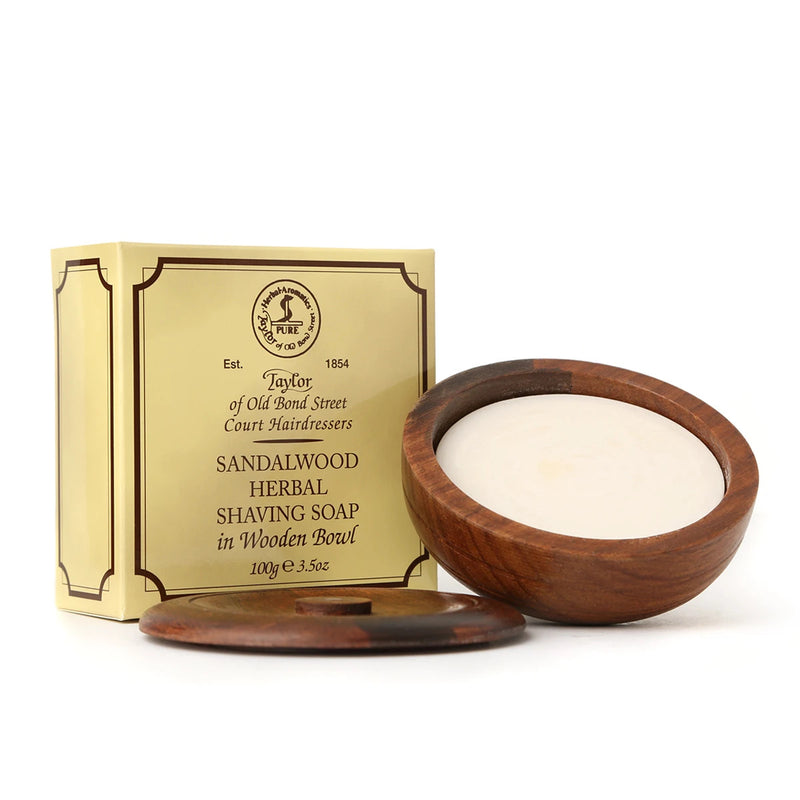 A Taylor of Old Bond Street Sandalwood Wooden Shave Bowl in an acacia wood bowl next to its packaging box labeled "Taylor of Old Bond Street". The box has a vintage design.