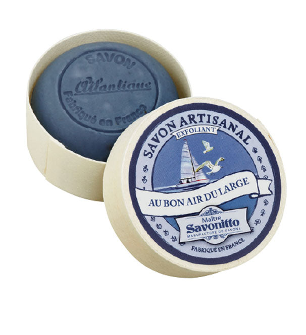 Round Maitre Savonitto Ocean Exfoliating Soap in an EA2G wooden box, featuring French labels and an illustration of a sailboat on a blue sea background. The text highlights natural ingredients like grape seed oil and sweet almond oil.