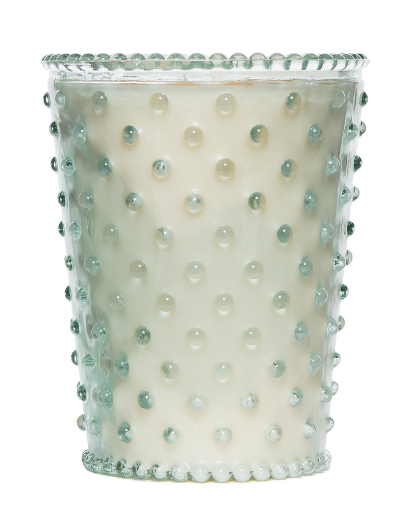 A Simpatico NO. 26 Scotch Pine Hobnail Glass Candle holder with raised dots, containing an off-white soy and vegetable wax blend candle, isolated on a white background.