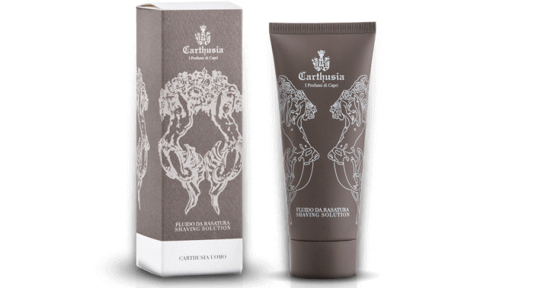 An image of a Carthusia I Profumi de Capri Salone da Barba Shave Solution tube next to its packaging box, both items are adorned with intricate, silvery gray designs featuring classical motifs and essential for the perfect shave.