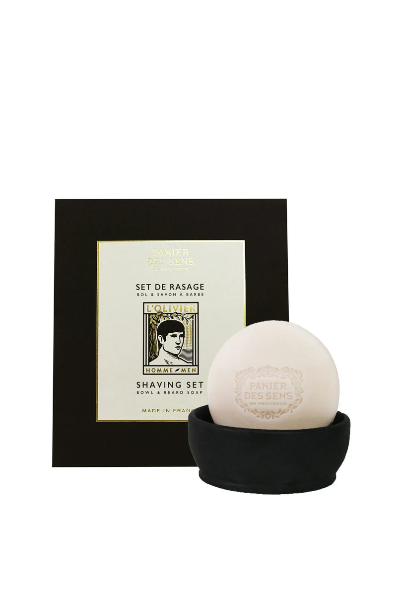 A Panier Des Sens L’Olivier Shaving Set, including a bar of beard soap in a black bowl, displayed in front of its beige and black packaging box with text and logos.