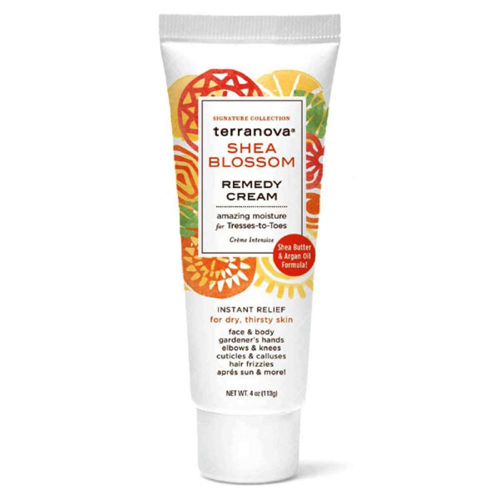 A tube of Terra Nova Shea Blossom Remedy Cream Amazing Moisture For Tresses-To-Toes with colorful orange and yellow floral designs. The packaging highlights its dry skin relief benefits and mentions key ingredients like shea butter and argan oil.