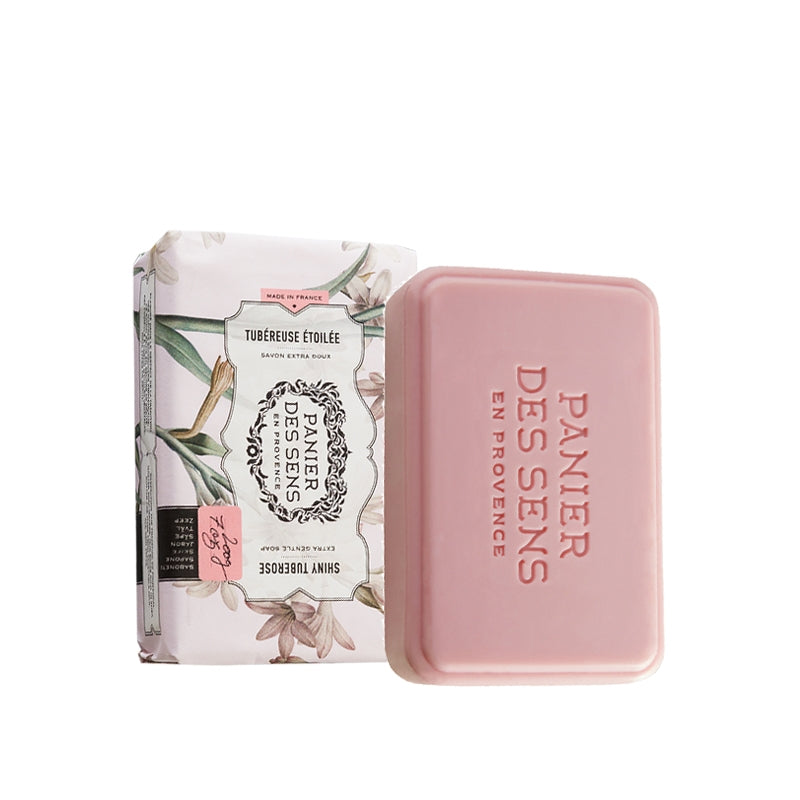 A pink bar of Panier Des Sens Extra-Soft Vegetable Soap - Shiny Tuberose next to its floral packaging, labeled "tuberuese etoilée" with text in both French and English.