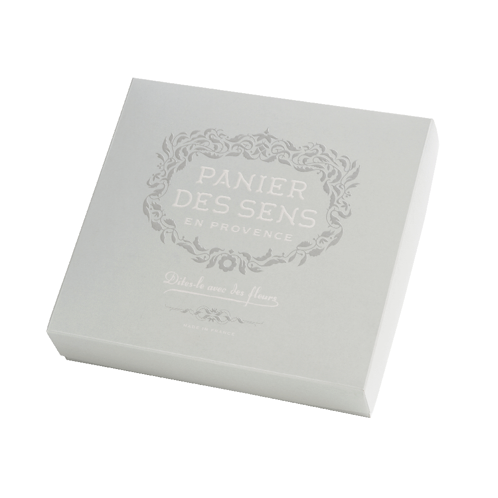 A square white Panier des Sens gift set box with a silver ornate logo that reads "panier des sens en provence" and French text underneath on its lid containing lavender essential oil.
