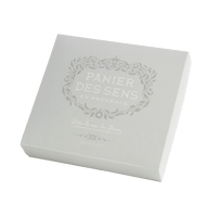 A square white Panier des Sens gift set box with a silver ornate logo that reads "panier des sens en provence" and French text underneath on its lid containing lavender essential oil.