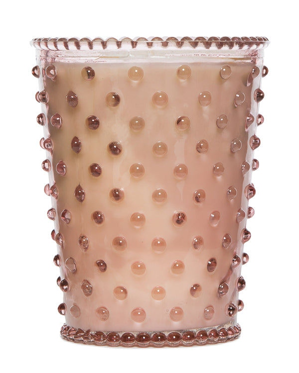 A textured Simpatico NO. 45 CORAL Hobnail Glass Candle filled with a creamy looking beverage with visible dark pearls scattered throughout, against a sunny citrus background.