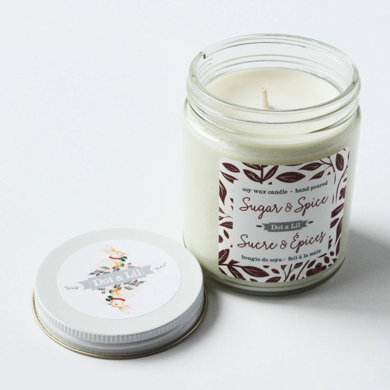 A hand-poured Dot & Lil Sugar + Spice Soy Candle in a clear glass jar with a matching lid, labeled "Sugar & Spice" with decorative floral graphics.
