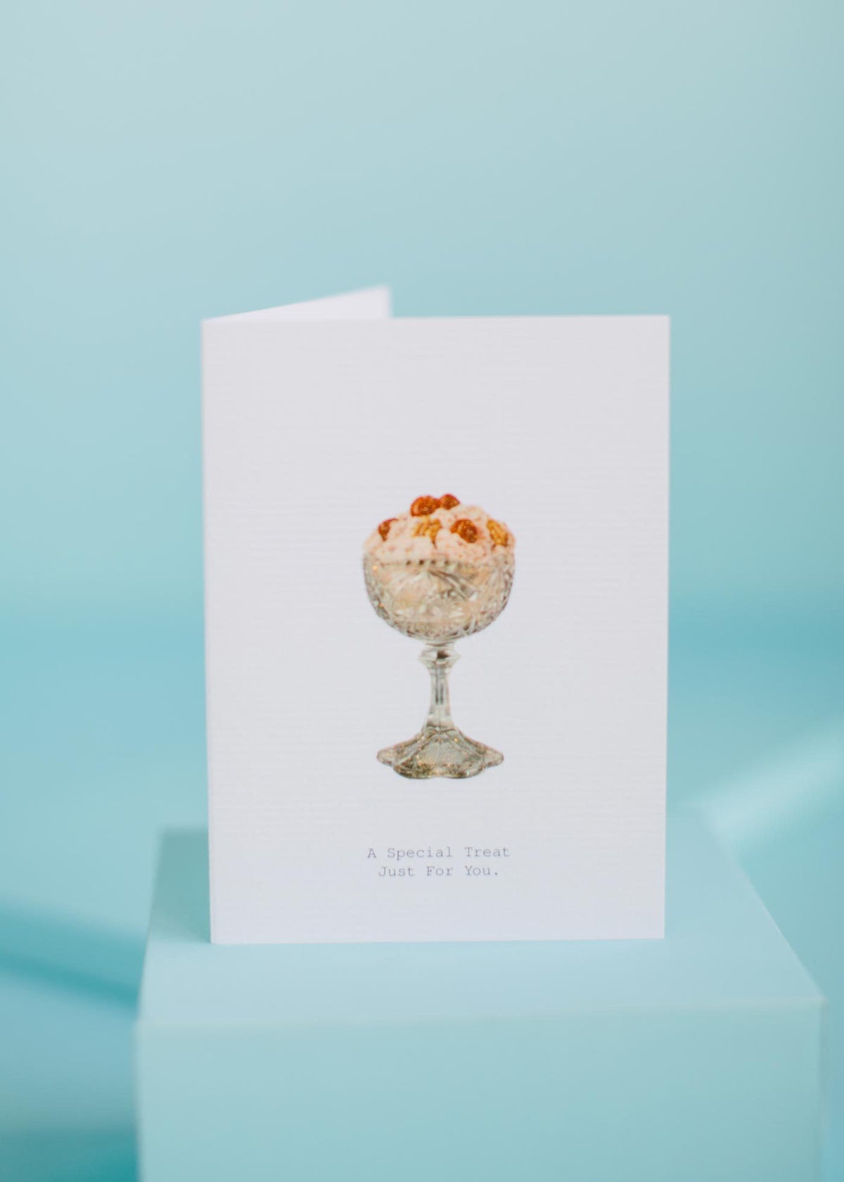 TokyoMilk Greeting Card - A Special Treat on a pale blue background featuring an image of a glass filled with a creamy dessert topped with nuts and the text "a special treat just for you," embellished with hand-glittered by Margot Elena.
