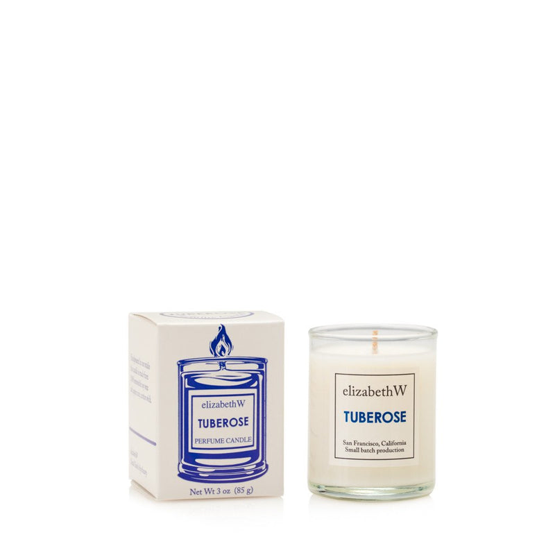 A elizabeth W Small Batch Apothecary Tuberose Candle - Petite in a clear glass container next to its matching white packaging box with blue and black text.