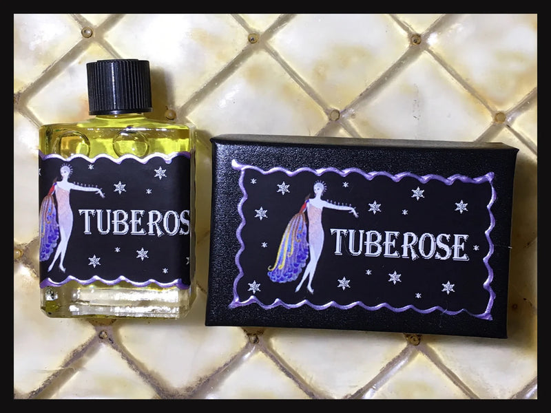 A bottle of Seventh Muse Fragrant Oil - Tuberose next to its black box, both featuring a design with a woman in a flowing dress against a starry background, on a tiled surface.