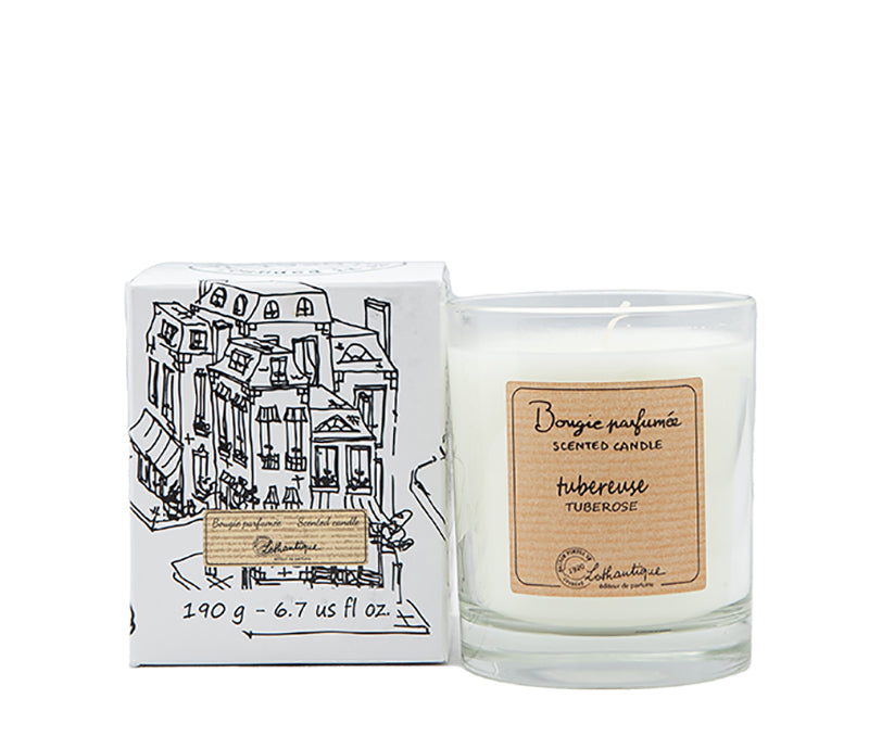 A Lothantique Tuberose Scented Candle made from mineral vegetable wax, in a clear glass jar, next to its packaging box with black and white illustrations of buildings.