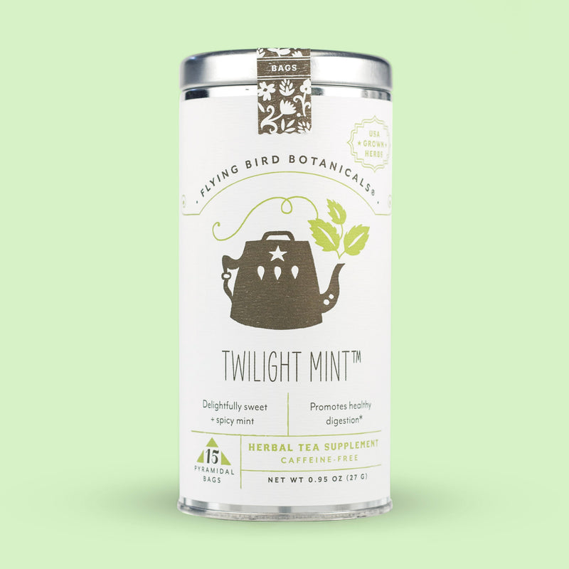 A canister of Flying Bird Botanicals' Twilight Mint herbal tea on a light green background. The canister is white with decorative designs and text about the Flying Bird Botanicals - Twilight Mint - 15 Tea Bag Tin, featuring organic spearmint and.