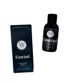 Product image of "Woolzies Unwind Essential Oil," a soothing clarity essential oil in a dark amber bottle next to its navy blue packaging box with white and light blue text.