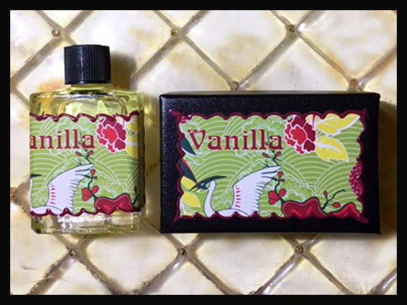 Two Seventh Muse Fragrant Oil - Vanilla products displayed on a tiled surface: on the left, a clear bottle filled with French perfume; on the right, a black rectangular box illustrated with floral designs.