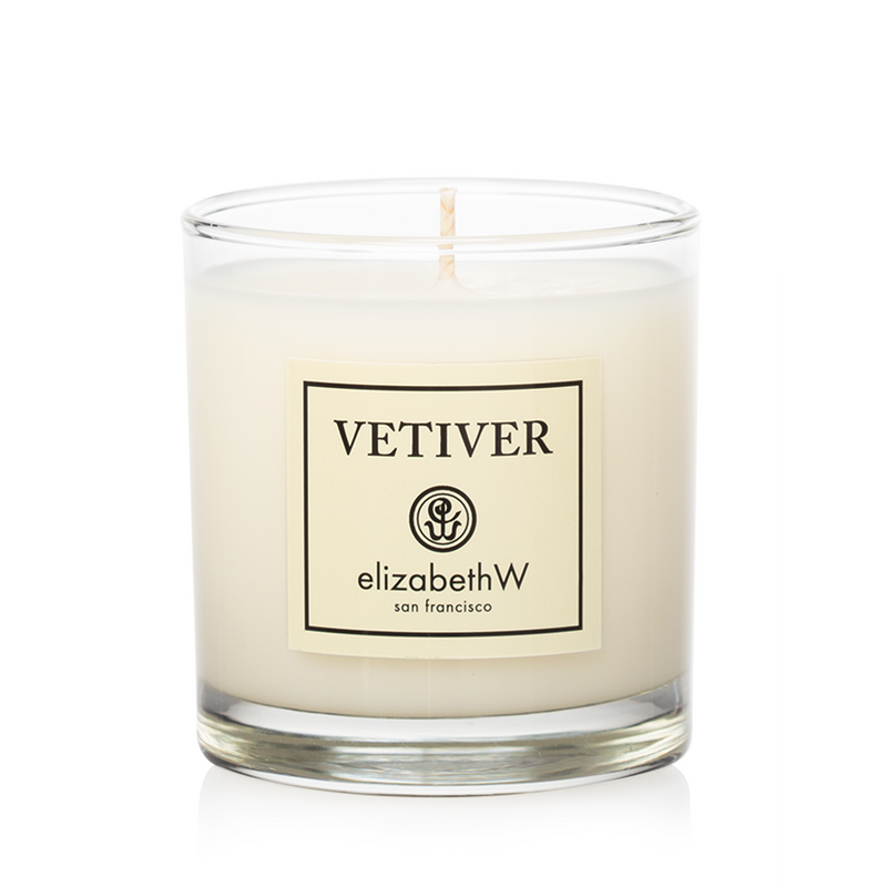 A soy wax candle in a clear glass container labeled "elizabeth W Signature Vetiver Candle," with the wick unlit and a white wax fill.