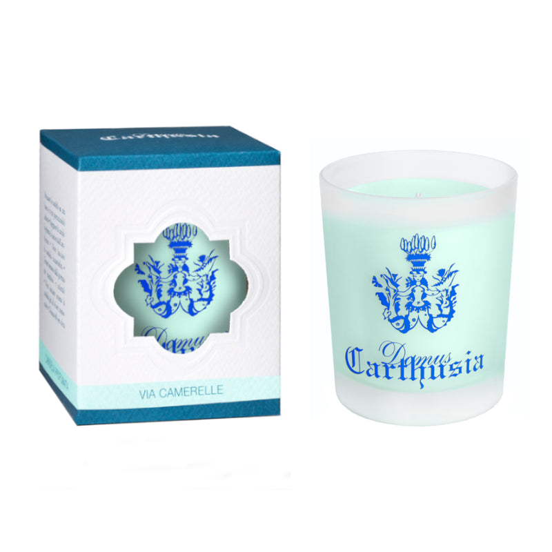 A Carthusia I Profumi de Capri Via Camerelle scented candle in a frosted glass engraved with subtle patterns, next to its packaging. The box is white with a heart-shaped cutout displaying the candle and blue detailing.