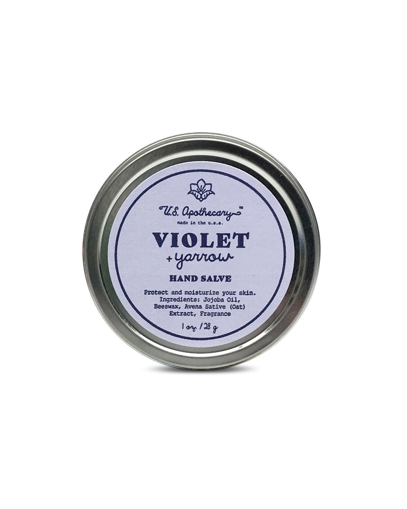 A tin container of "U.S. Apothecary Violet & Yarrow Hand Salve" with a simple purple and white label, emphasizing its moisturizing and protective qualities for sensitive skin. Now enhanced