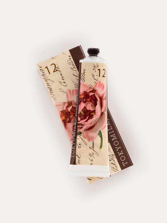 A Margot Elena beauty product in a floral, clock-themed packaging, symbolized by both elegance and time, infused with Japanese Green Tea - TokyoMilk Gin & Rosewater No. 12 Bon Bon Shea Butter Lotion, placed on a plain white background.
