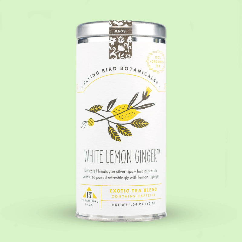 A cylindrical tea canister with an elegant design featuring illustrations of lemons and organic ginger root, labeled "Flying Bird Botanicals - White Lemon Ginger - 15 Tea Bag Tin" against a soft green background.