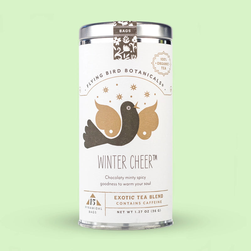 A tin of Flying Bird Botanicals - Winter Cheer - 15 Tea Bag Tin with a design featuring two birds, stars, and text detailing the organic peppermint, chocolate minty spicy flavor, against a pale green.