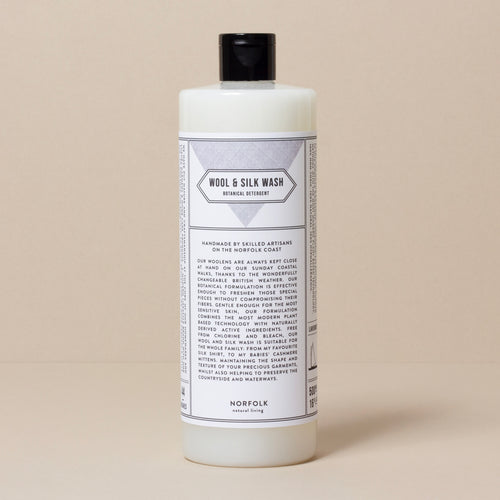 A bottle of Norfolk Natural Living Lavender Wool & Silk Wash detergent on a neutral beige background, featuring detailed care instructions and ingredients listed on the label. This detergent is enhanced with botanical formulation designed for sensitive skins.